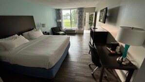 A hotel room with a bed, desk, chair, TV, and a view of the outdoors.