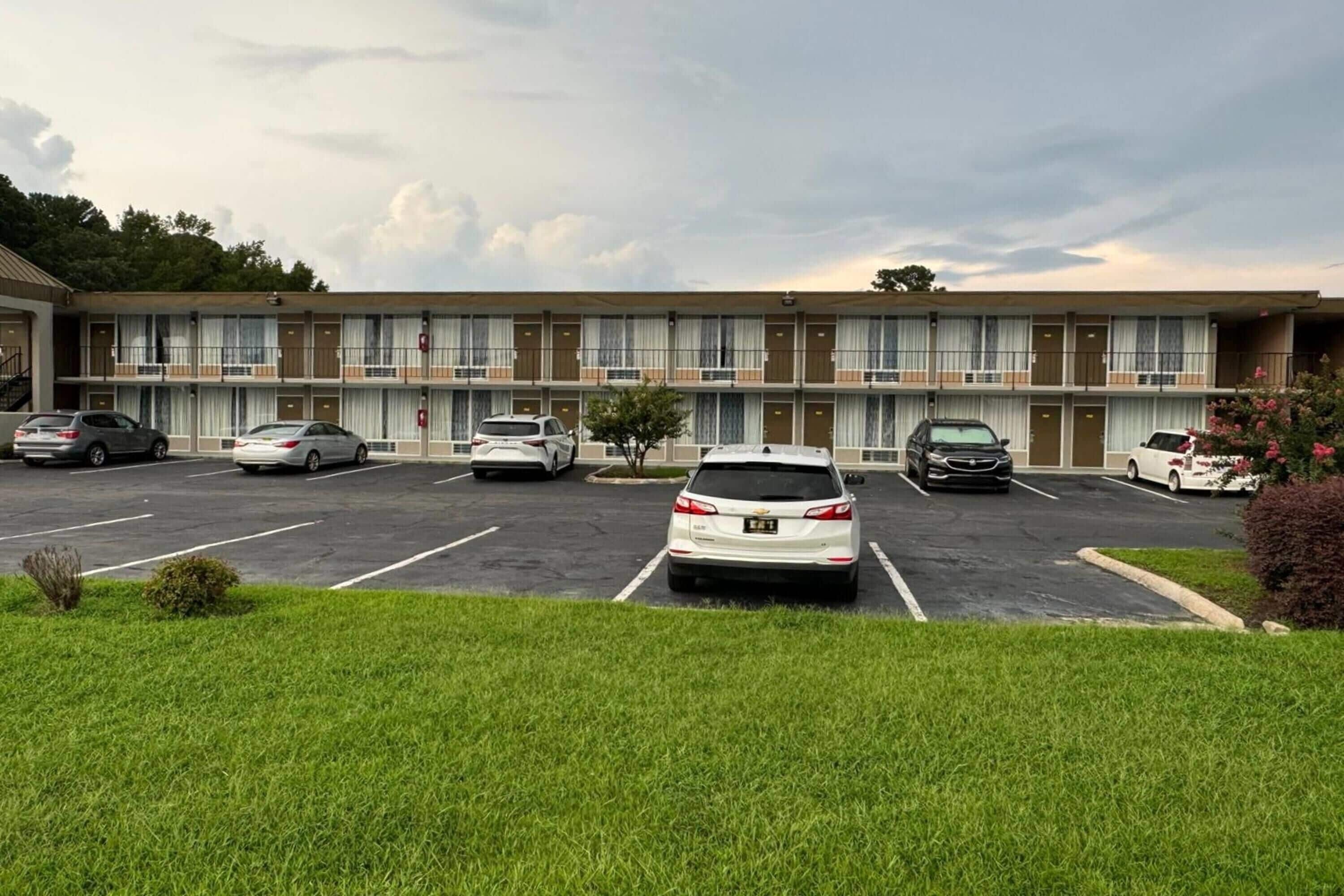 A motel with a parking lot, multiple cars, and a grassy area in front.