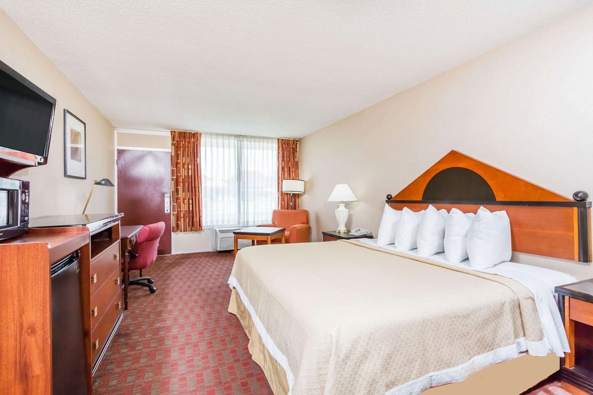 A hotel room with a bed, desk, chair, TV, and a window with curtains.