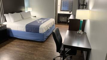A hotel room with a bed, desk, chair, and a lamp.