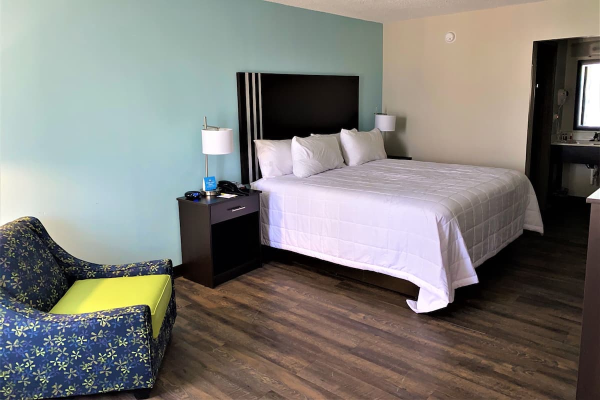 A hotel room with a bed, bedside tables, a chair, a desk, and a television.