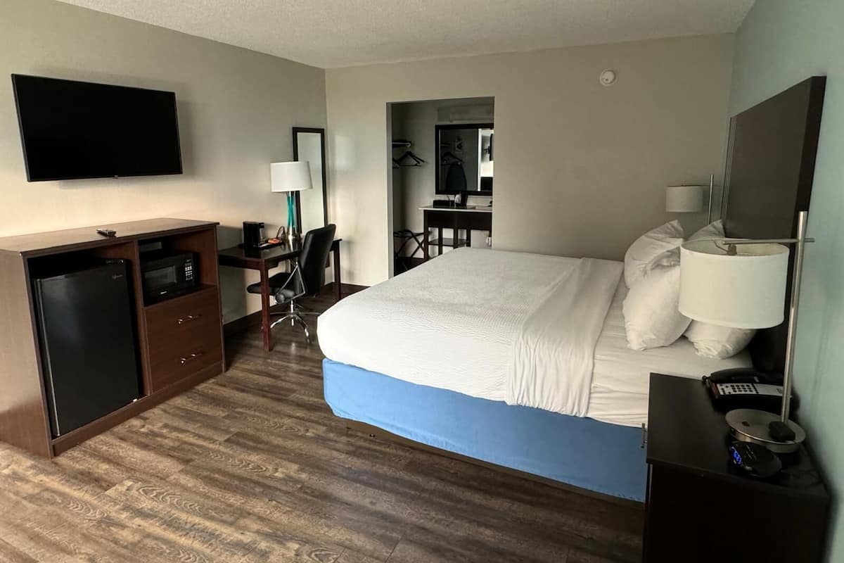 A hotel room with a bed, a desk, a chair, a TV, and a minibar.