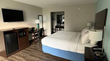 A hotel room with a bed, a desk, a chair, a TV, and a minibar.