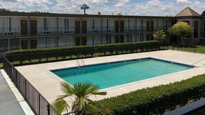 A hotel with a swimming pool, a covered outdoor area, and a row of rooms with balconies.
