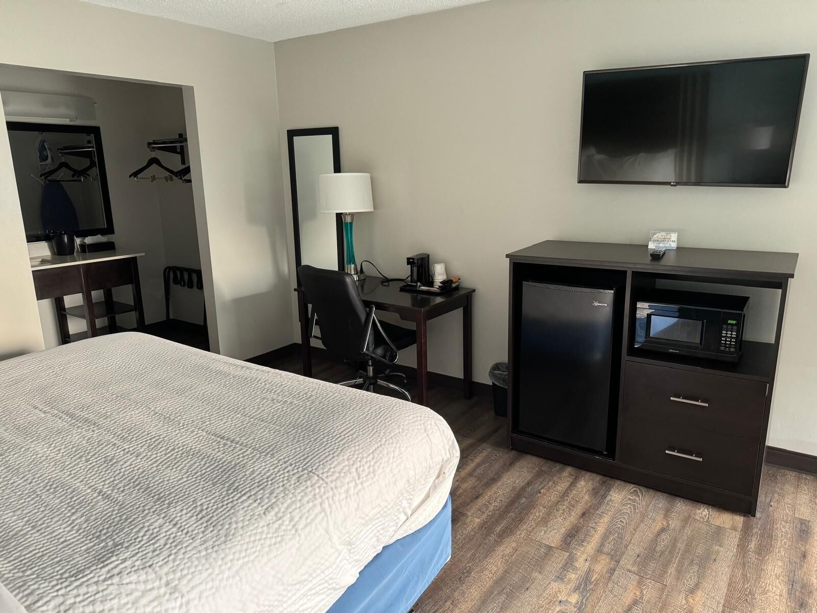 A hotel room with a bed, a desk with a computer, a microwave, and a TV.