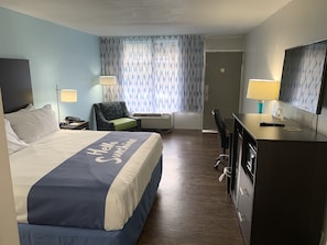 A hotel room with a bed, a desk, a chair, a desk lamp, a wall-mounted TV, and a window with patterned curtains. - Days Inn by Wyndham Goldsboro (Goldsboro)