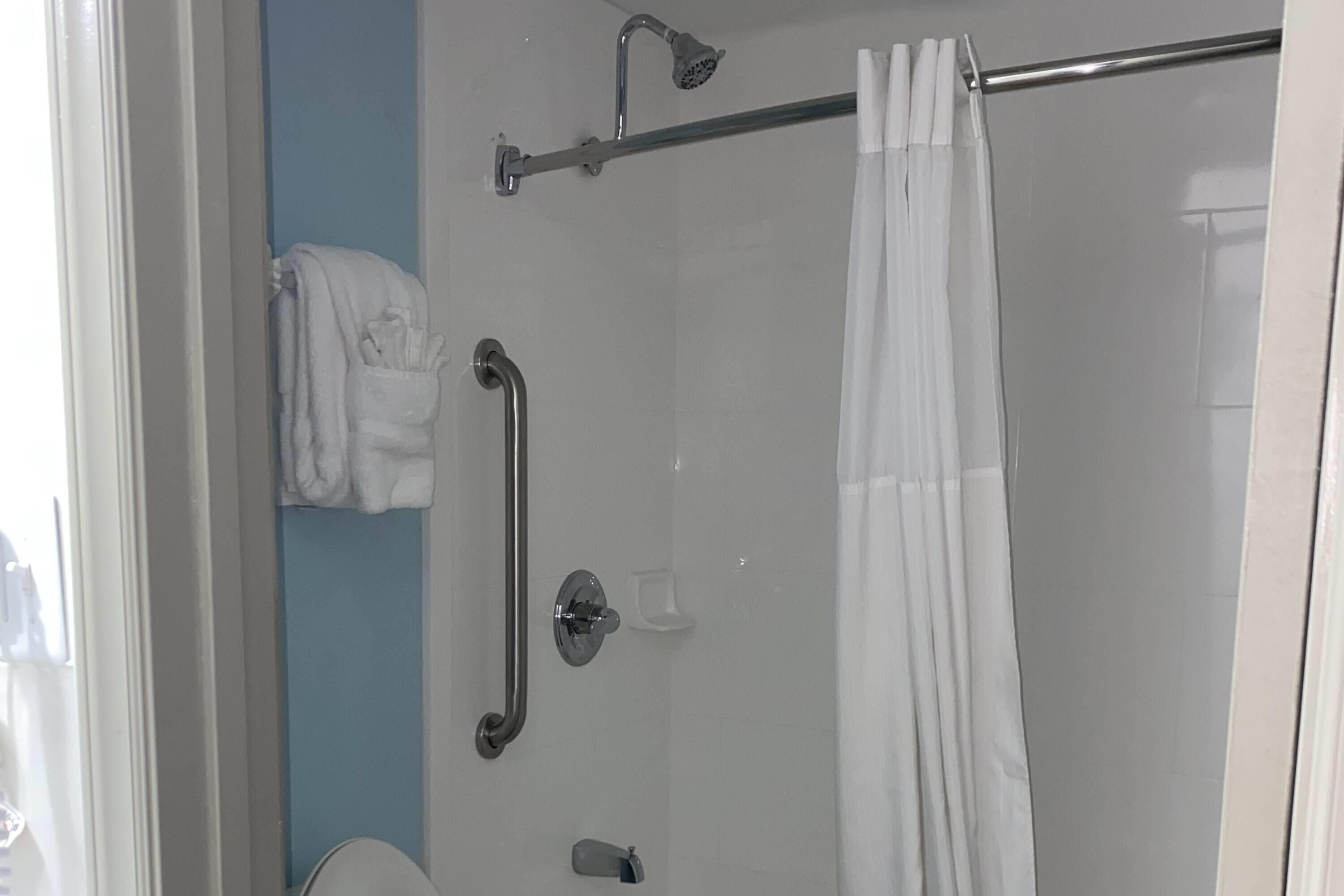 A bathroom with a glass shower enclosure, a towel rack, and a handrail.