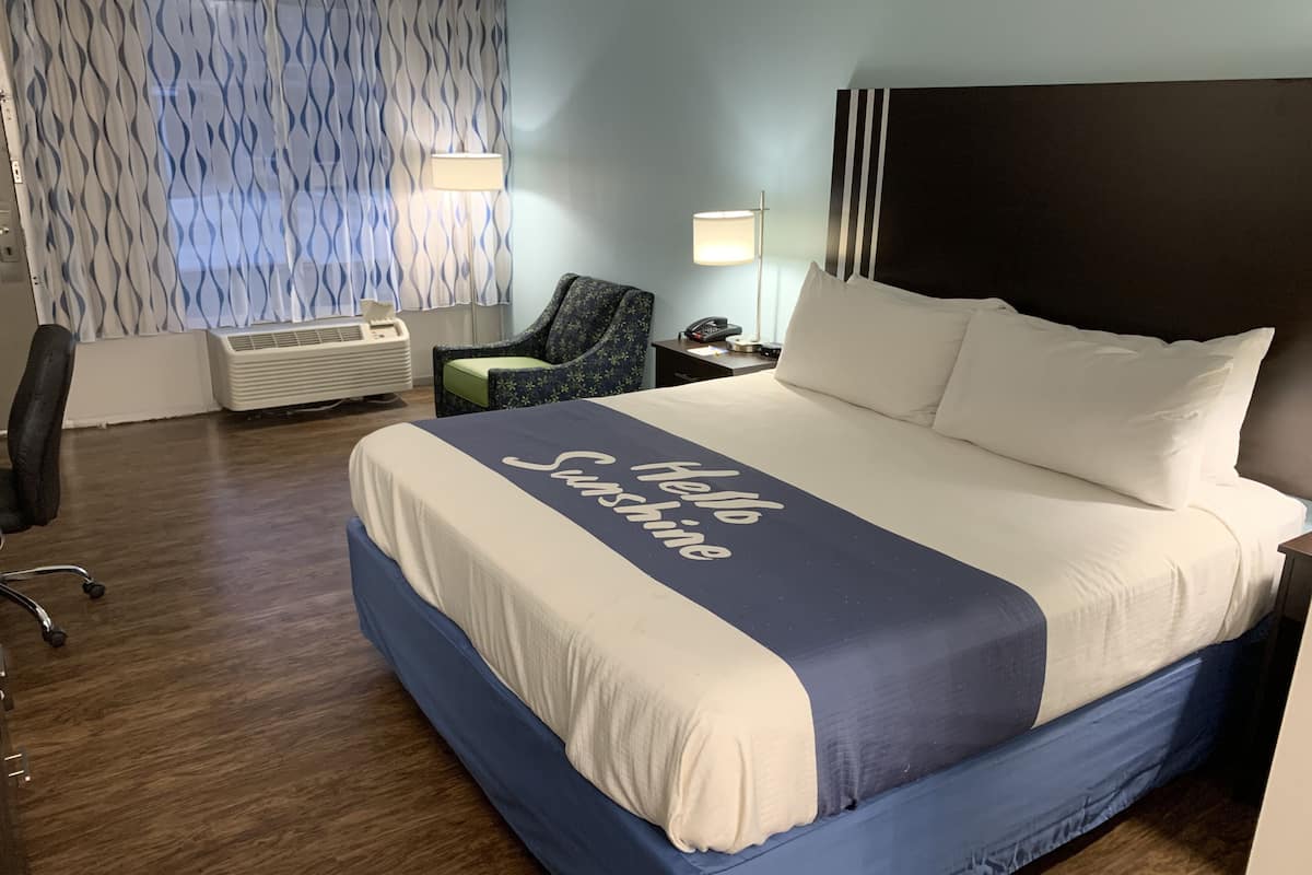 A hotel room with a large bed, a chair, a desk with a lamp, and a window with curtains.