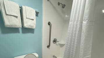 Un baño con inodoro, ducha con barra de apoyo y dos toallas colgadas en una pared.