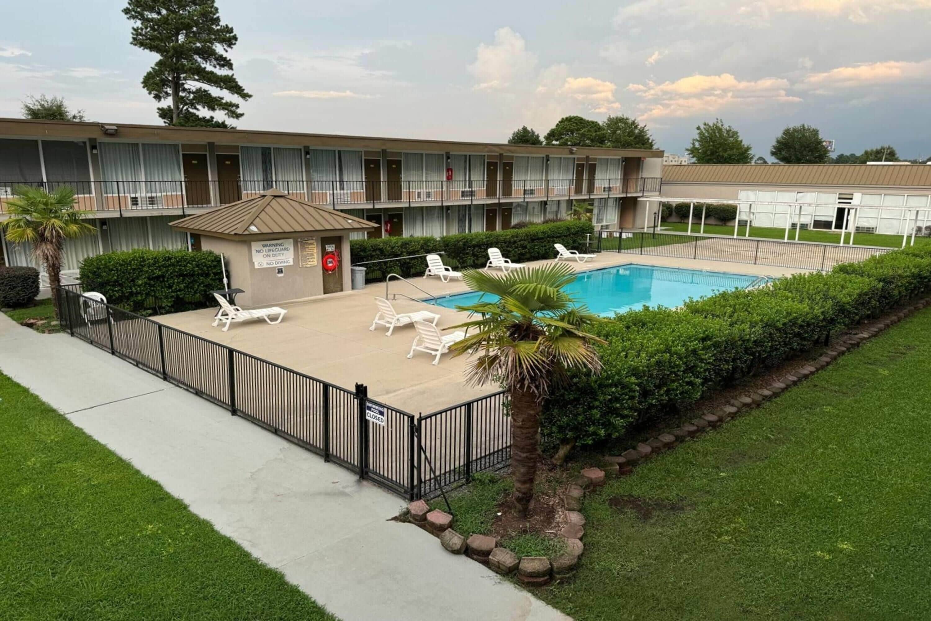 A motel with a swimming pool, lounge chairs, and a fenced patio area.