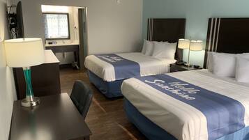 A hotel room with two beds, each with a 'Hello Sunshine' bedspread, a desk with a lamp, a chair, and a small table.