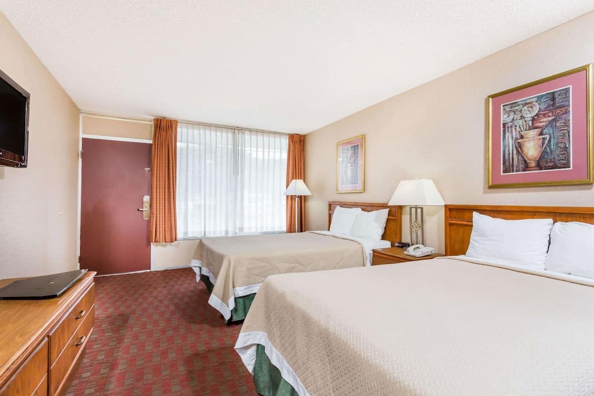 A hotel room with two beds, a desk with a laptop, a telephone, and a painting on the wall.