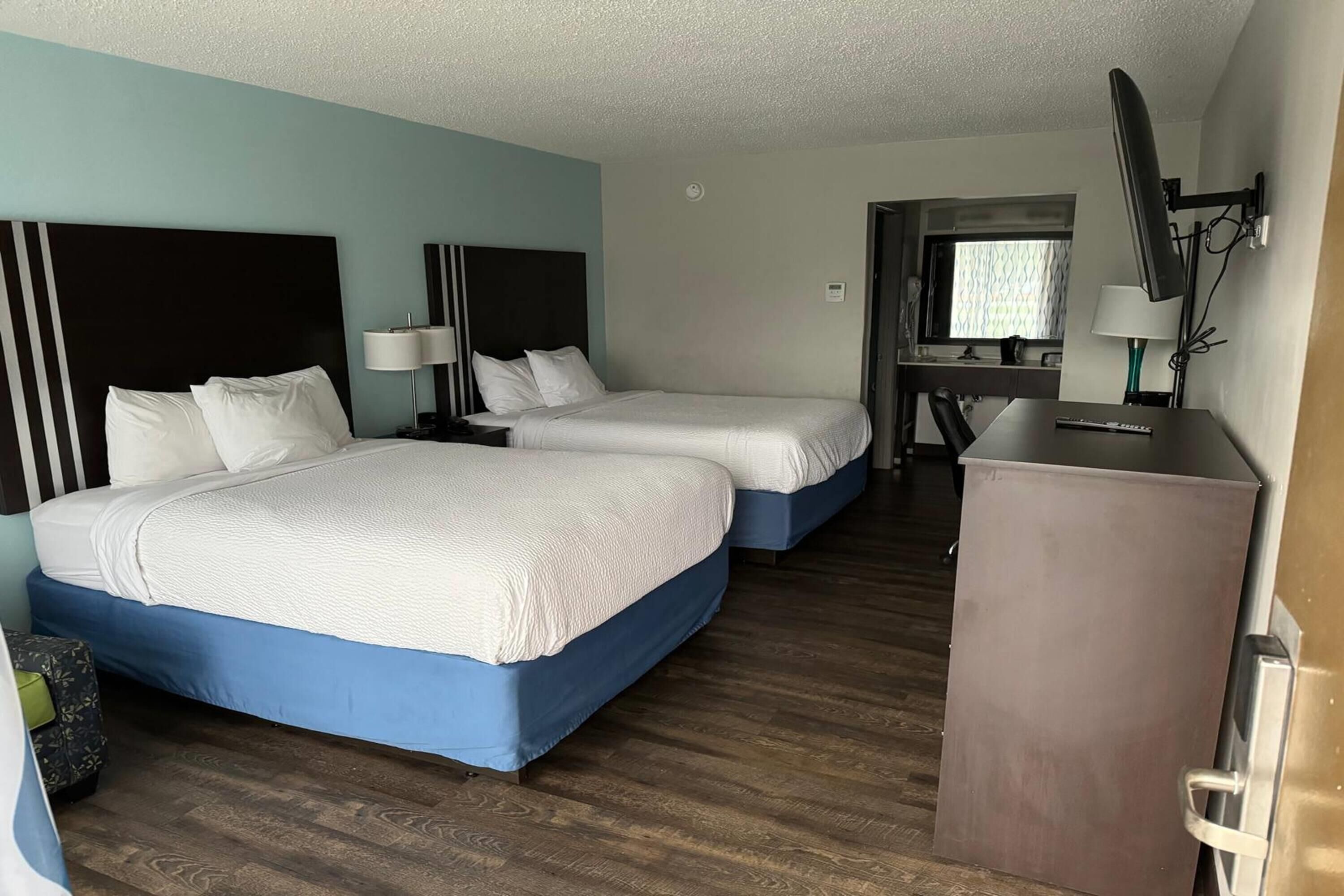 A hotel room with two beds, a desk, a mirror, and a television.