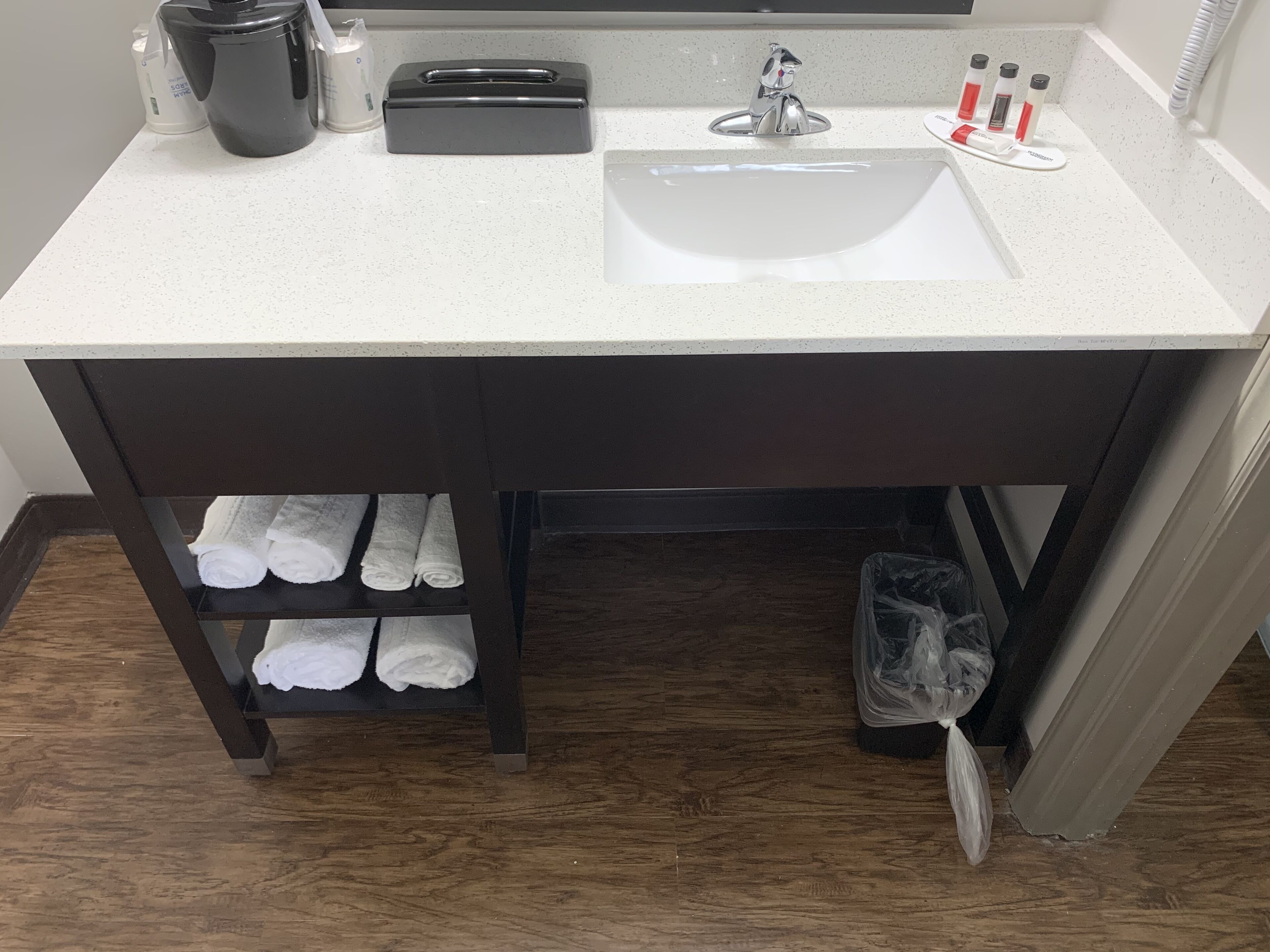 A bathroom with a white sink, dark wooden vanity, and a shelf with folded towels.