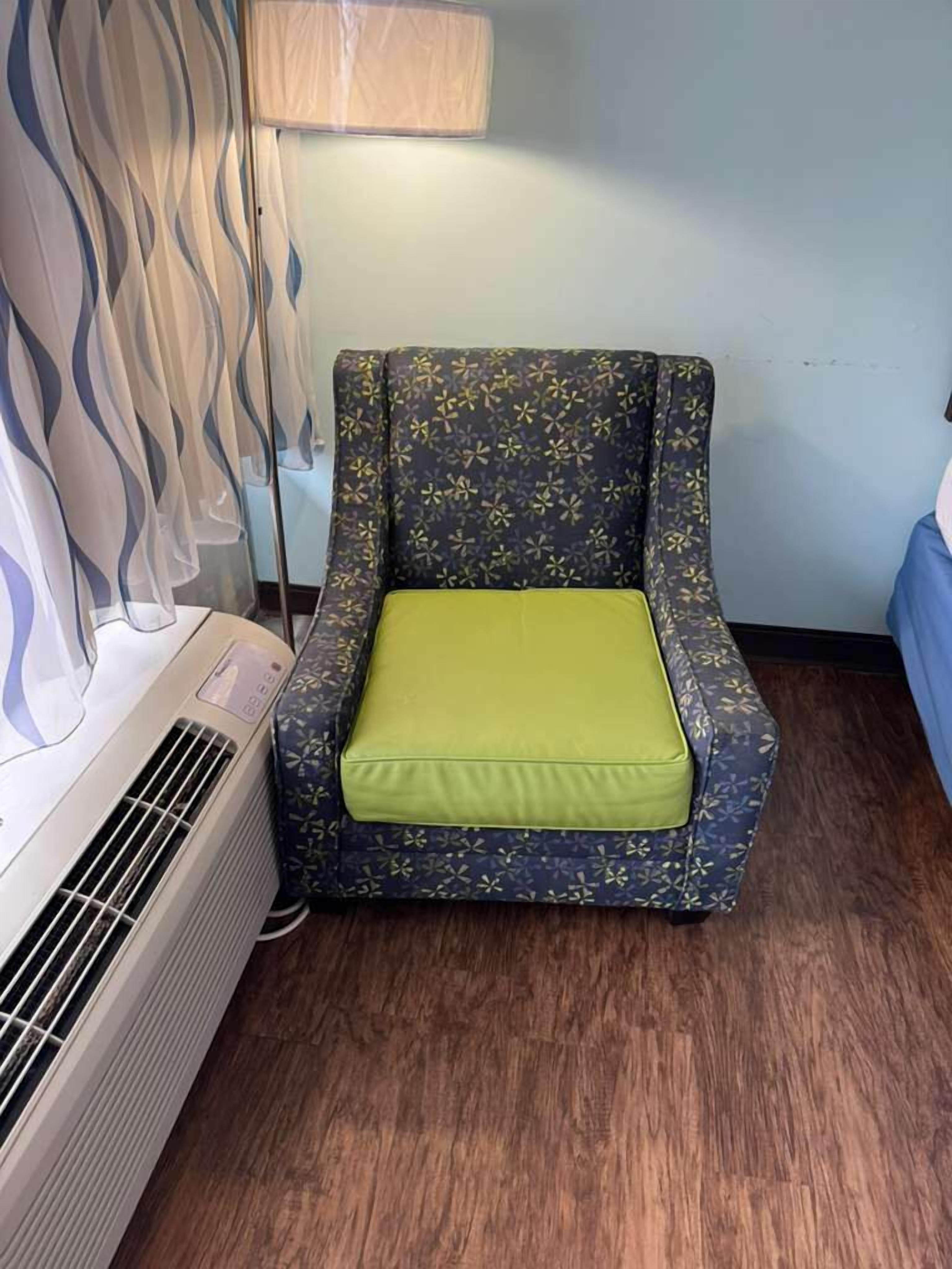 Una habitación con un sillón estampado, un calentador portátil y una cortina.