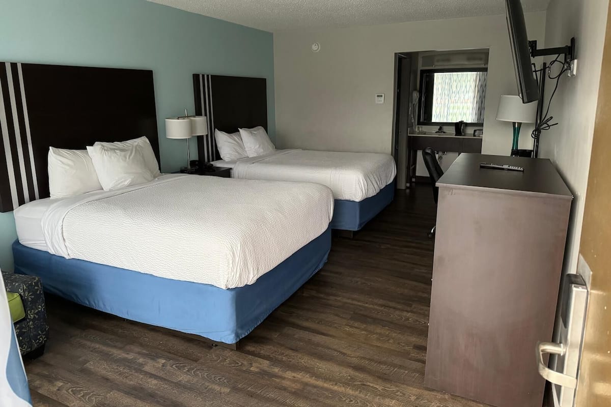 A hotel room with two beds, a desk, a mirror, and a TV.