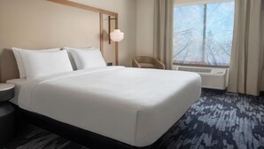 Hotellihuone, jossa on suuri sänky, yöpöytä, tuoli, ikkuna verhoilla ja ilmastointilaite.
