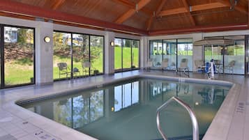 An indoor swimming pool with clear glass walls, a tiled floor, and a wooden ceiling.