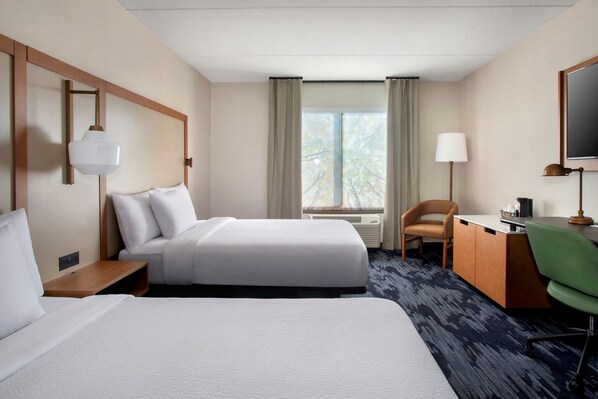 A hotel room with two beds, a desk, a chair, a lamp, and a large window with curtains.