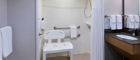 A bathroom with a shower, a white chair, a towel rack, and a sink.