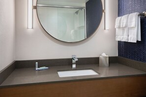 A bathroom with a round mirror, a sink, a towel rack, and a tissue box.