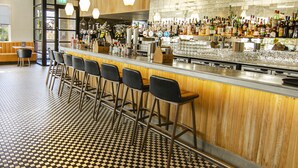 A bar area with a checkered floor, wooden bar counter, and multiple stools. - Strathaven Hotel (Strathaven)
