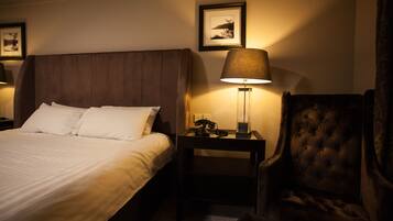 A hotel room with a large bed, a nightstand with a lamp, a chair, and framed pictures on the wall.