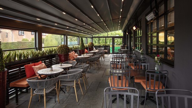 An outdoor cafe area with multiple tables and chairs, potted plants, and a view of the surrounding greenery. - Strathaven Hotel (Strathaven)
