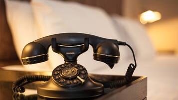 A vintage black telephone on a bedside table in a hotel room.