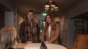 A man and a woman standing in a room with a table, chairs, and a chandelier. - Strathaven Hotel (Strathaven)