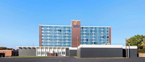 A Comfort Inn hotel with a modern glass facade, a parking lot in front, and a clear blue sky.