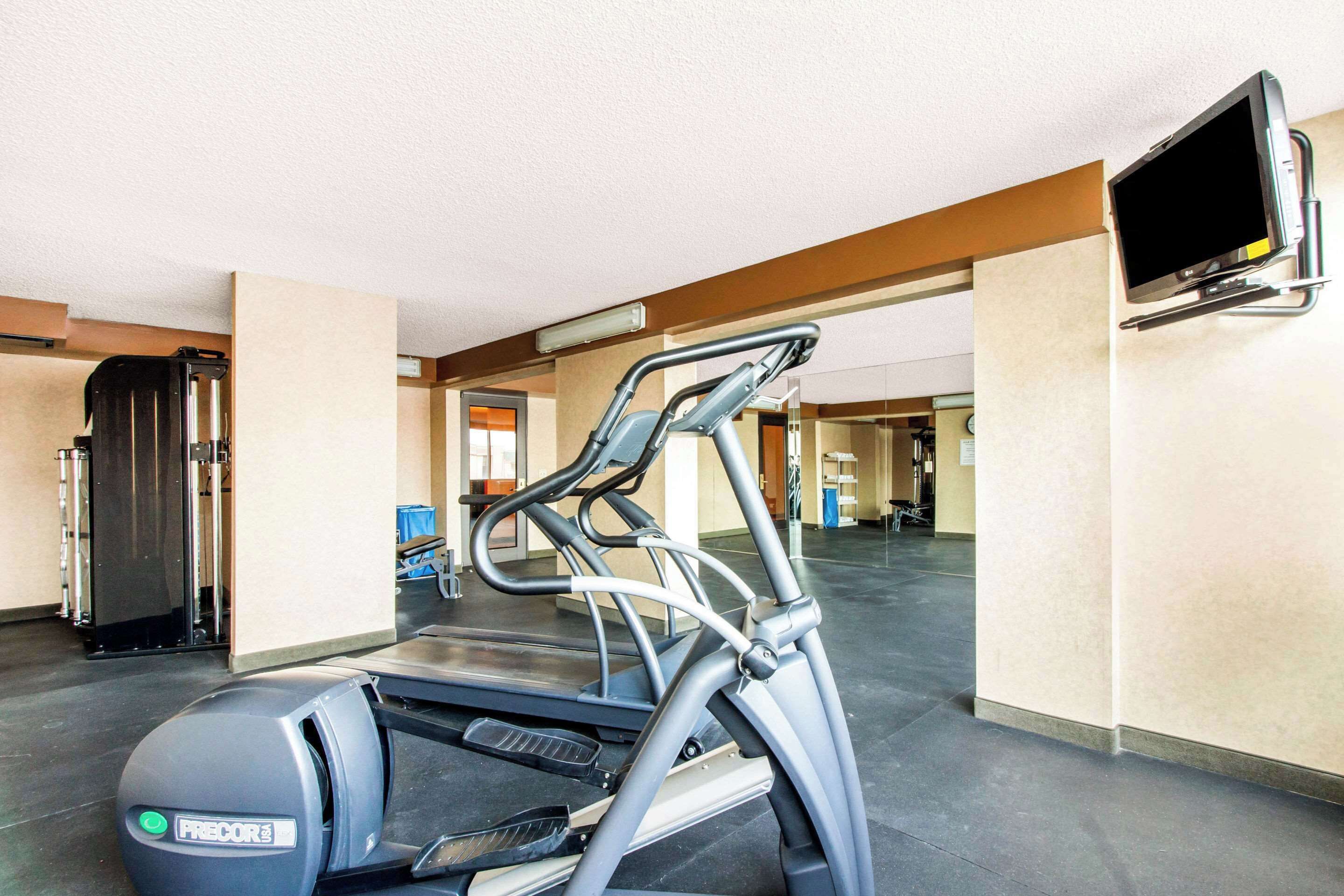 A gym with a treadmill, a stationary bike, and a television mounted on the wall.
