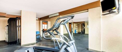 A gym with a treadmill, a stationary bike, and a television mounted on the wall.