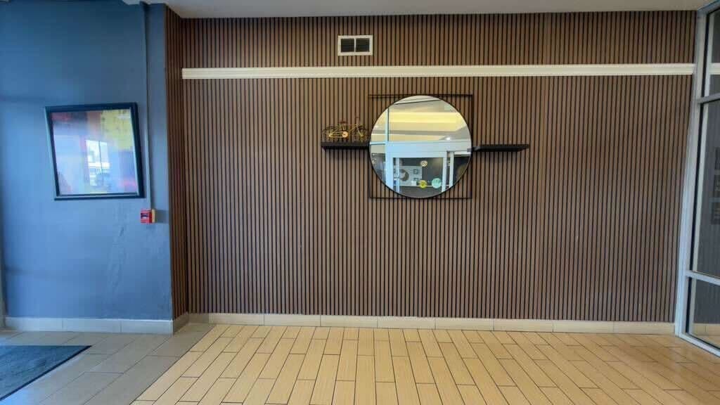 Una habitación con pared de paneles de madera, un espejo redondo y un cuadro enmarcado a la izquierda.