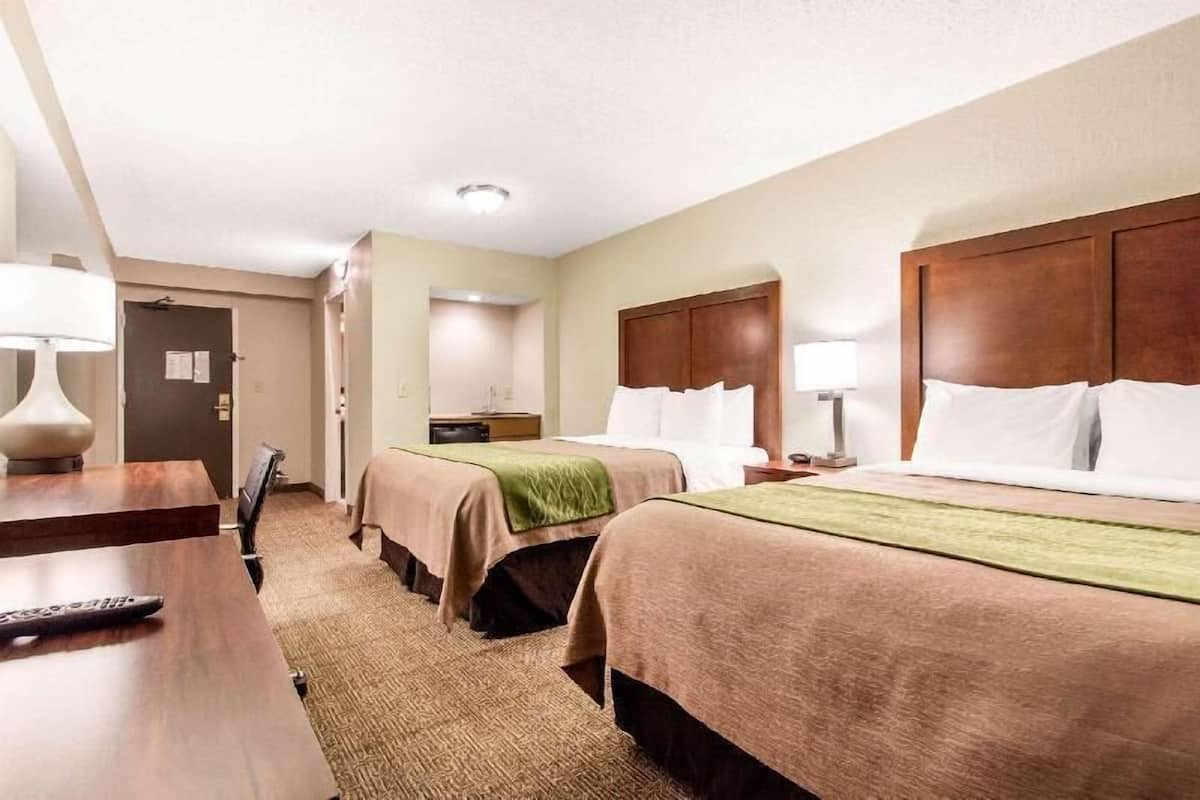 A hotel room with two beds, a desk, a chair, a lamp, and a door.