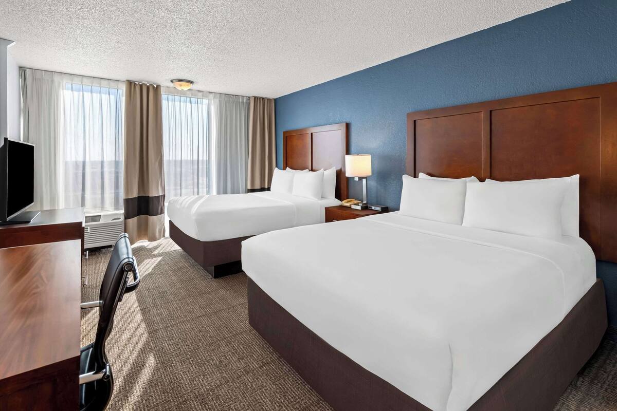 A hotel room with two beds, a desk, a TV, and a window with curtains.