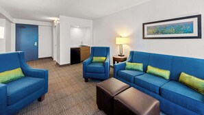 A hotel room with a blue sofa set, a small table, and a lamp. There is a painting on the wall and a door in the background. - Comfort Inn & Suites Omaha Central (Omaha)