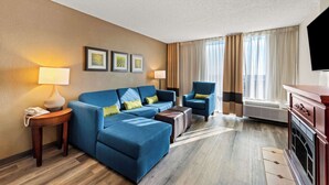 A hotel room with a blue sofa, a chair, a small table with a lamp, a TV, and a fireplace. - Comfort Inn & Suites Omaha Central (Omaha)