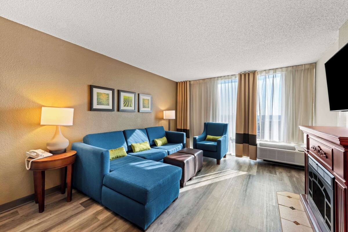 A hotel room with a blue sofa, a chair, a small table with a lamp, a TV, and a fireplace.