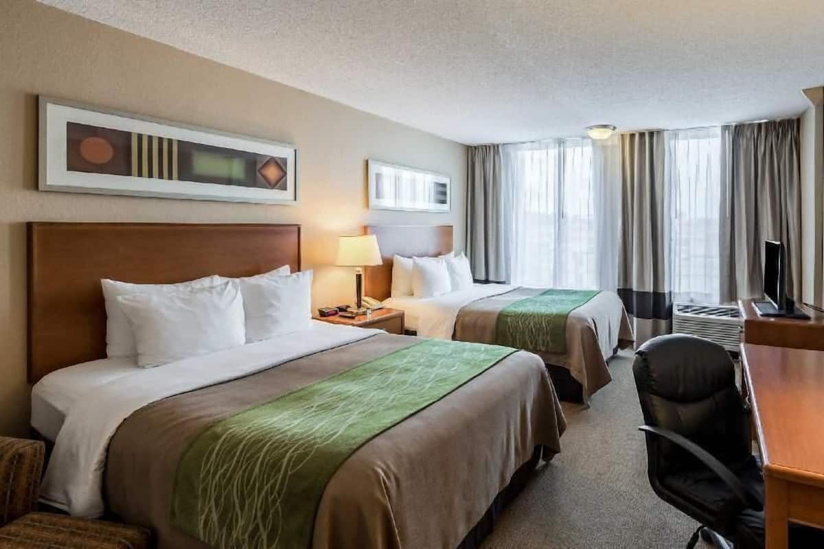 A hotel room with two beds, a desk, a chair, a TV, and a window with curtains.