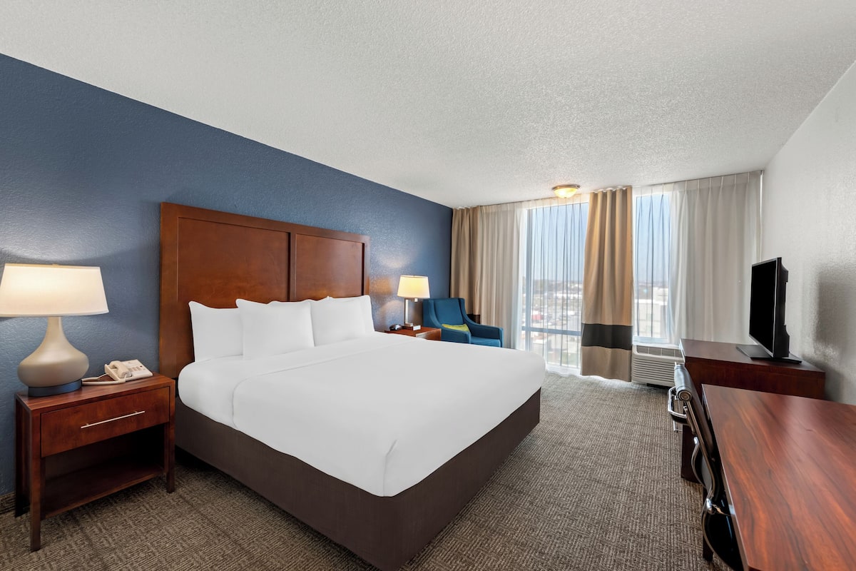 A hotel room with a large bed, a desk, a chair, a TV, and a window with curtains.