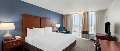 A hotel room with a large bed, a desk, a chair, a TV, and a window with curtains.