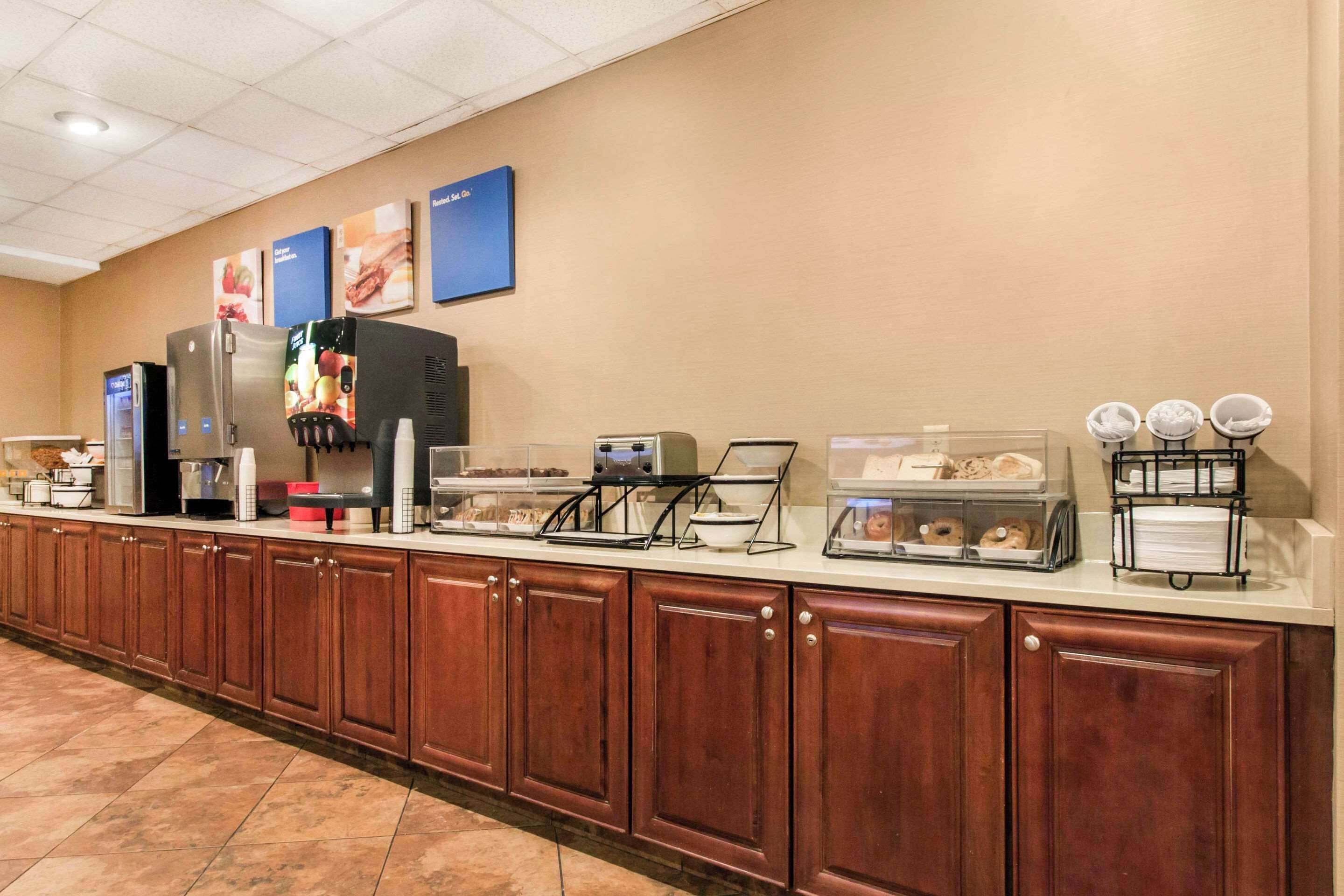 Un mostrador de desayuno de hotel con refrigerador, cafetera y distintas vitrinas de comida.
