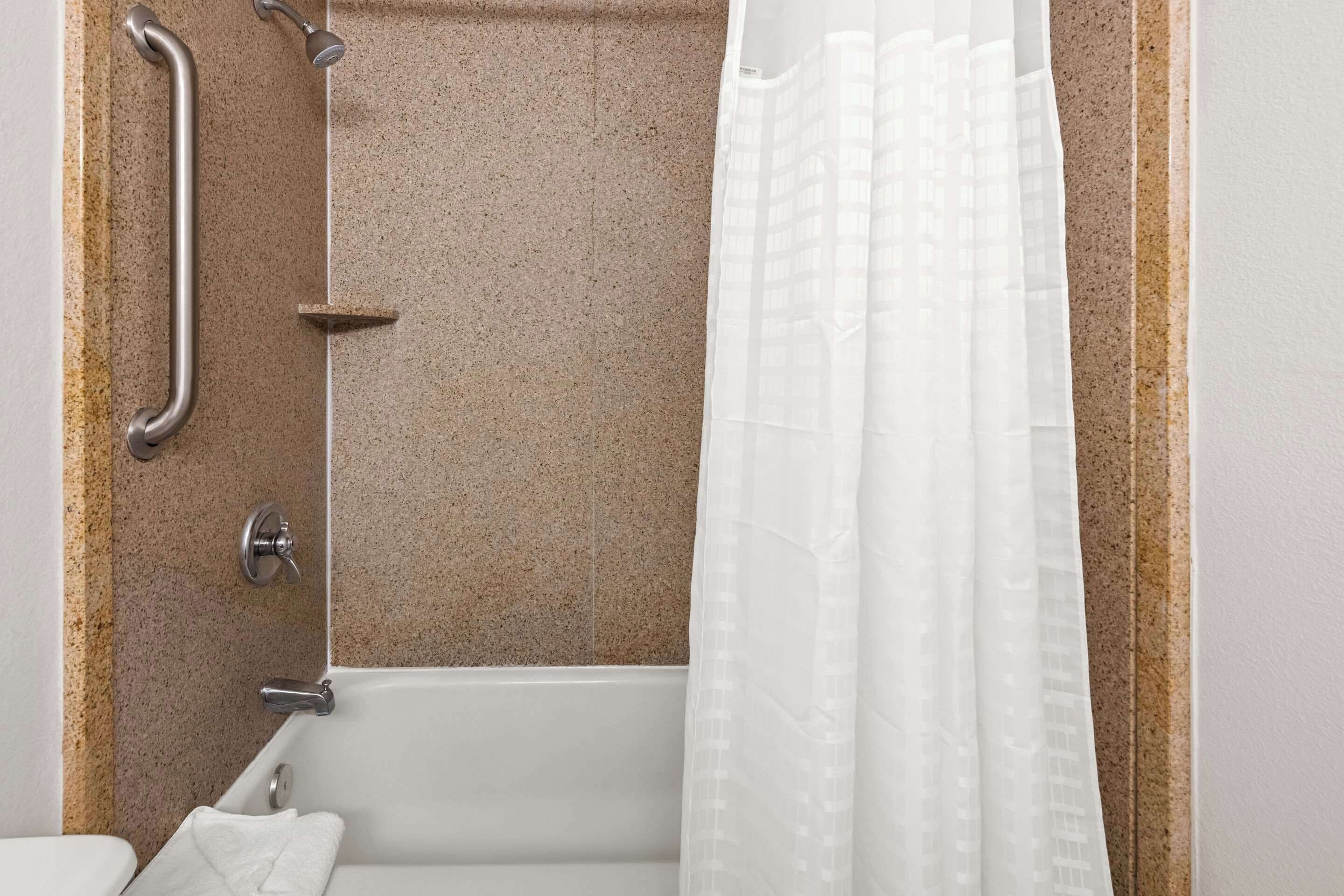 Baño con bañera, barras de apoyo y cortina de ducha.