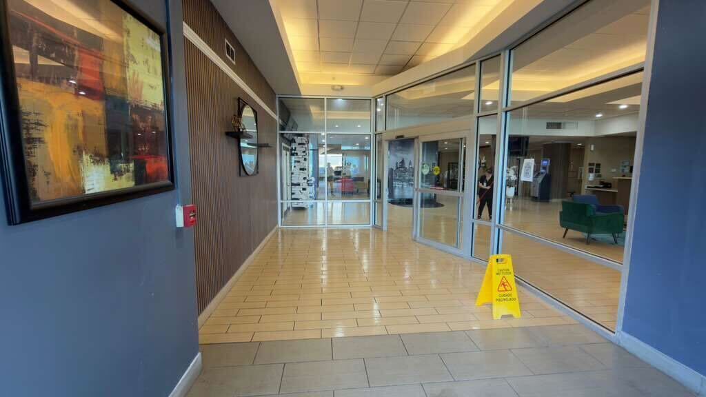A hallway with a wooden floor, glass doors, and a yellow caution sign.