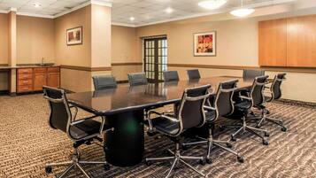 A conference room with a large table and eight chairs, carpeted floor, wooden panel walls, and a door in the background.