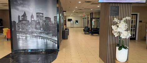 A lobby with a large digital display of a city skyline, a reception desk, and a potted plant.