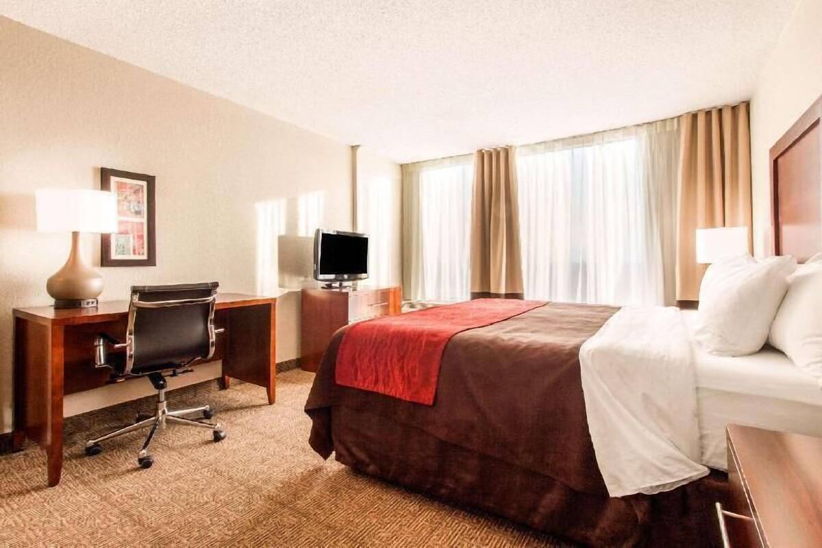 A hotel room with a bed, desk, chair, television, and curtains.