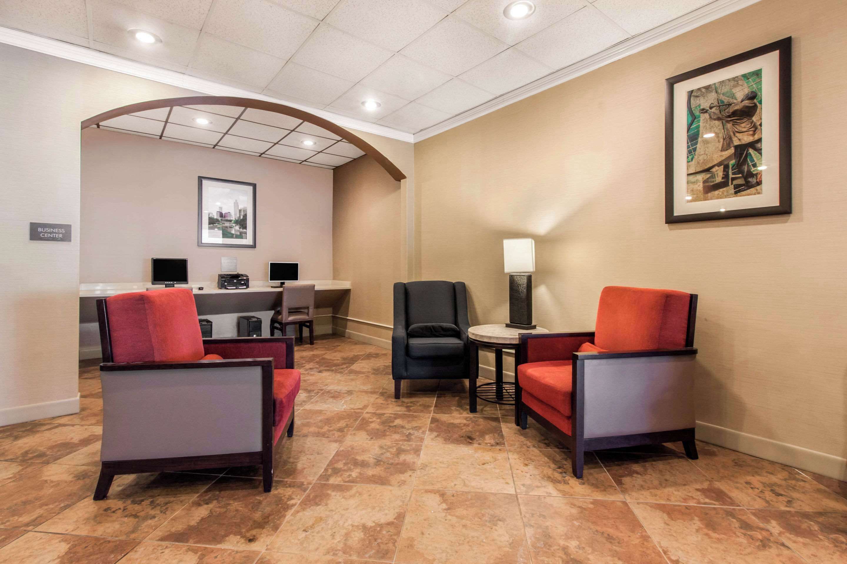 A hotel lobby with a reception desk, two armchairs, a small table, and a framed artwork on the wall.