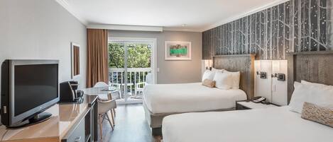 Habitación de hotel con dos camas, televisión, escritorio y balcón con vista a árboles.
